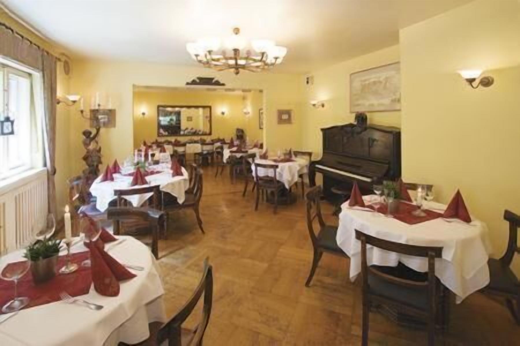 Un comedor con mesas dispuestas para comidas, un piano y una araña.