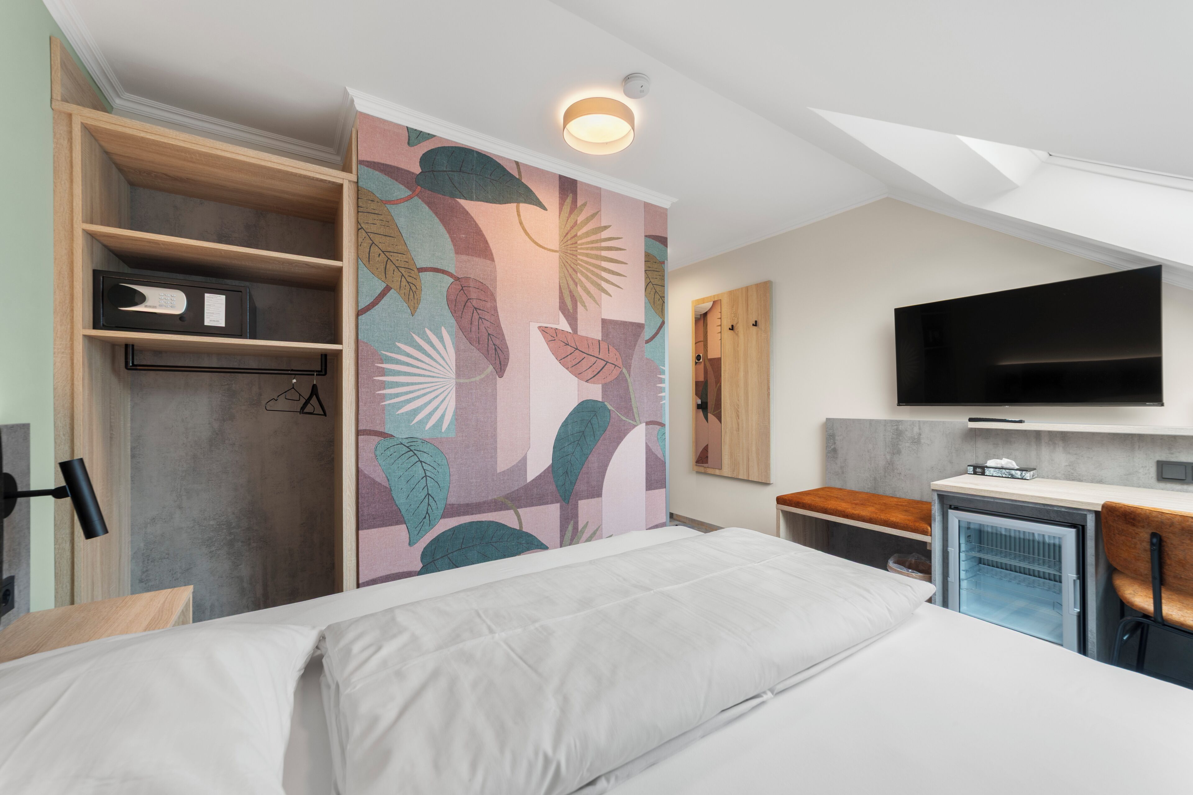 A modern hotel room with a bed, a wardrobe, a small fridge, and a flat-screen TV.