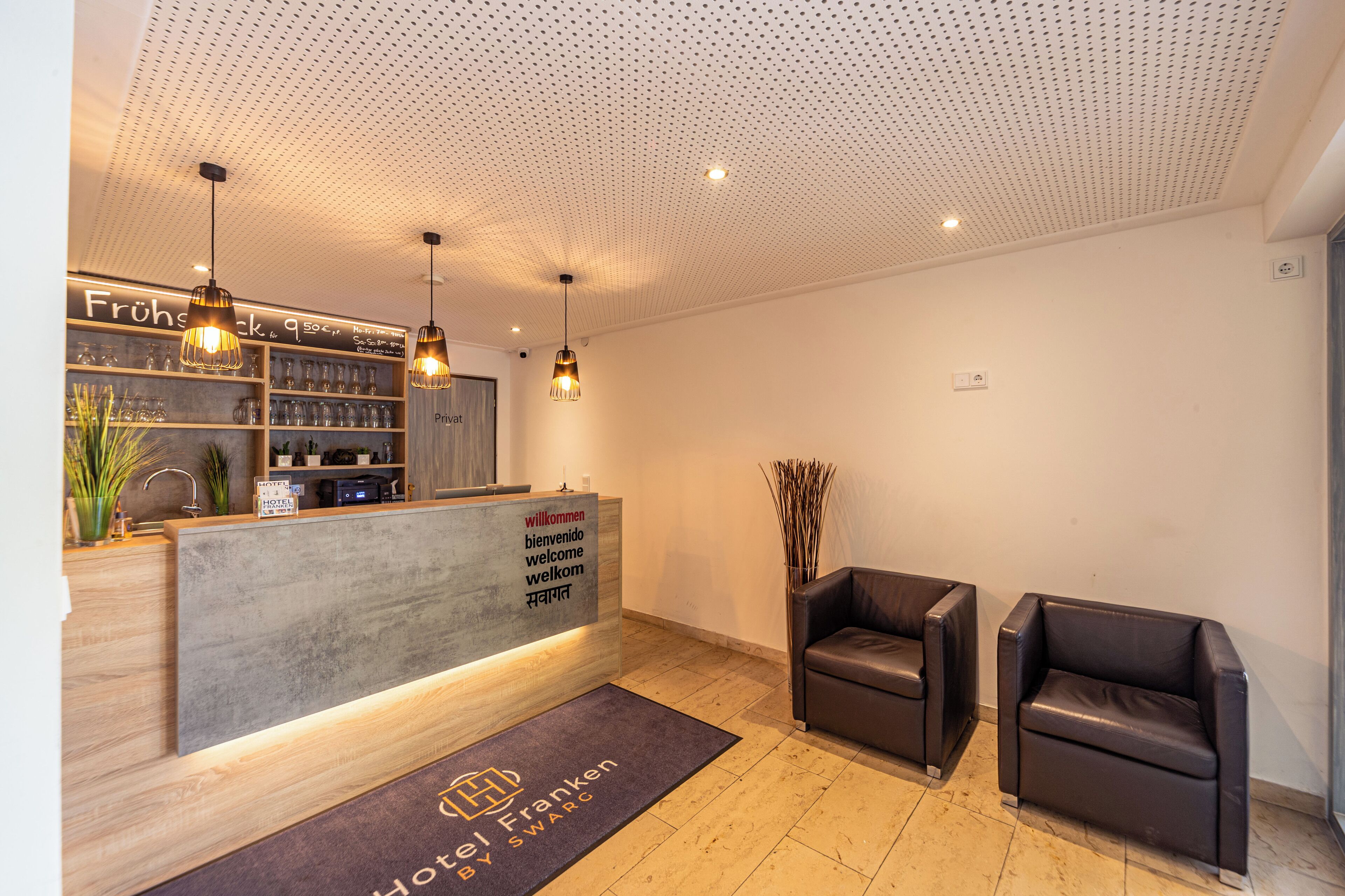 Zona de recepción de hotel con diseño moderno, que incluye mostrador de recepción, espacio de estar y un minibar a la vista.