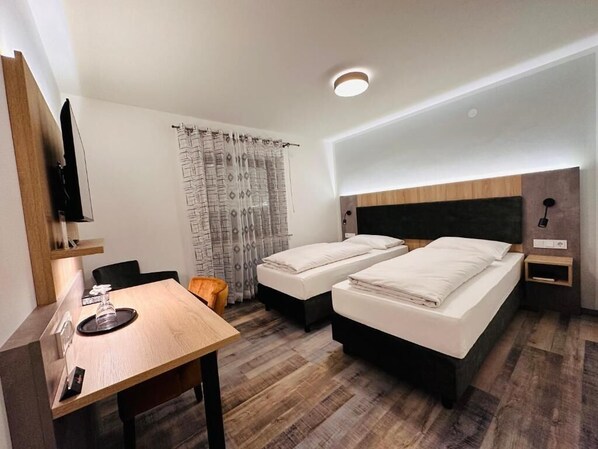 A hotel room with two beds, a desk, a TV, and a curtain. - Hotel Franken (Forchheim)