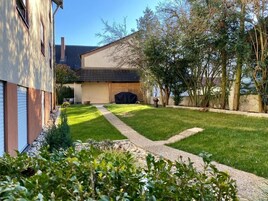 Um imóvel residencial com gramado bem cuidado, um caminho que leva à casa e uma área de churrasqueira coberta.
