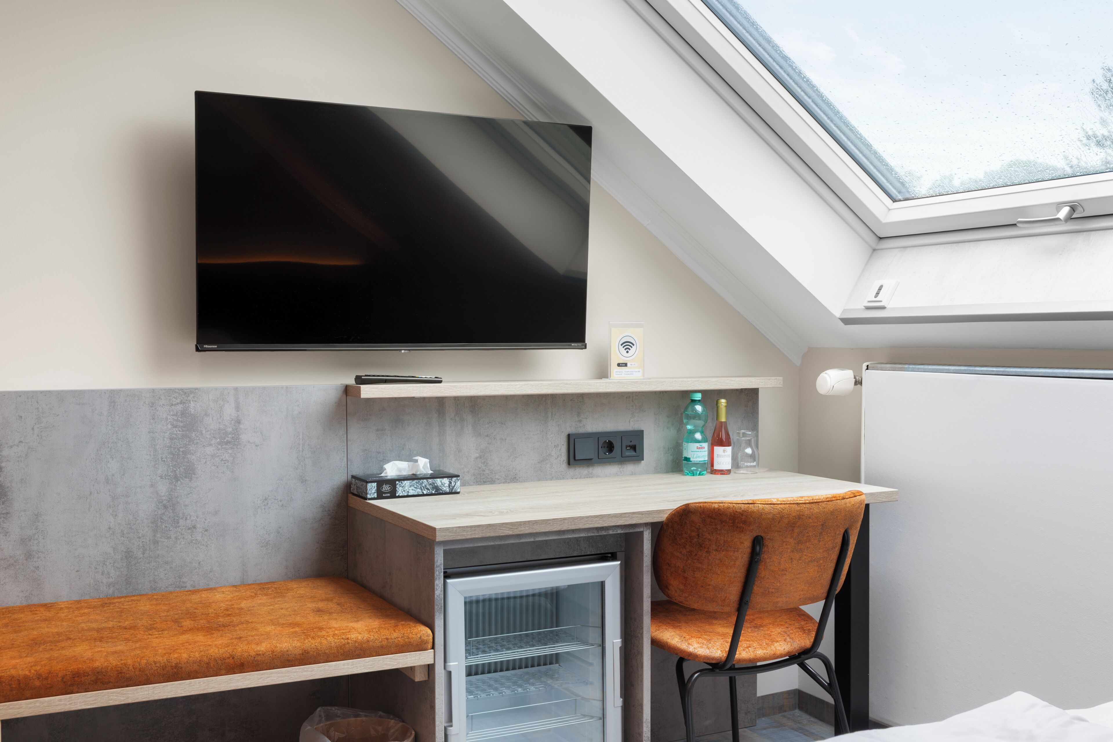 Habitación compacta con televisión de pantalla plana, pequeña kitchenette, una silla y un mini refrigerador integrado.