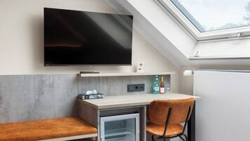 Habitación compacta con televisión de pantalla plana, pequeña kitchenette, una silla y un mini refrigerador integrado.