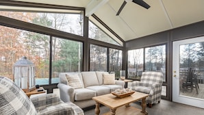 A cozy living room with a sofa, armchairs, and a coffee table. Large windows offer a view of trees and a gazebo. - The Poolside Escape | Hot Tub | Arcade | Ping Pong (Bridgman)