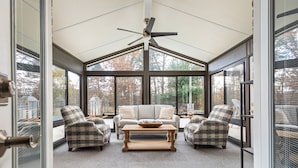 A sunroom with a ceiling fan, large windows, a sofa, two armchairs, and a coffee table. - The Poolside Escape | Hot Tub | Arcade | Ping Pong (Bridgman)