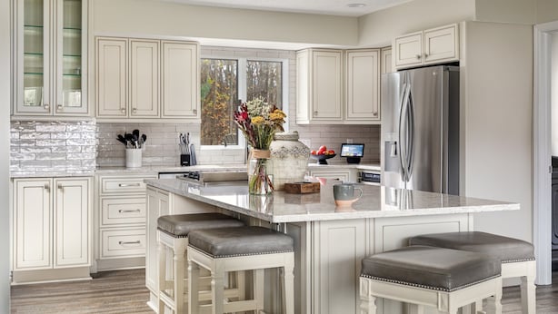 A modern kitchen with white cabinetry, a large island with bar stools, a stainless steel refrigerator, and a window with a view of trees. - The Poolside Escape | Hot Tub | Arcade | Ping Pong (Bridgman)