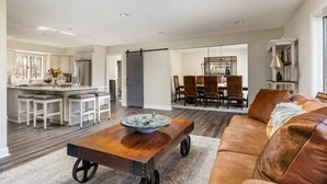 A spacious living area with a wooden coffee table, a brown leather sofa, and a dining area with a chandelier. - The Poolside Escape | Hot Tub | Arcade | Ping Pong (Bridgman)