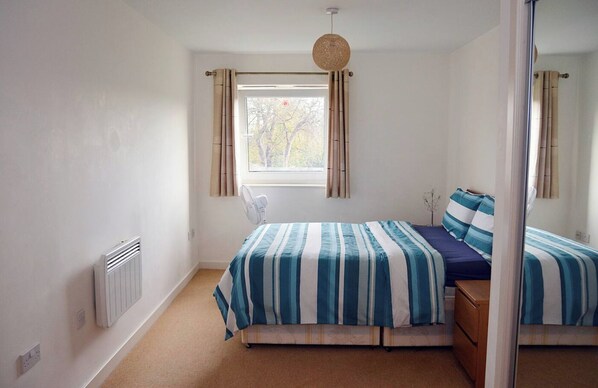 A bedroom with a bed, a window, a radiator, and a bedside table.