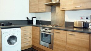 Eine kleine Küche mit Holzausstattung, einem Edelstahlherd, einem Einbauofen, einer Waschmaschine und einem Toaster.