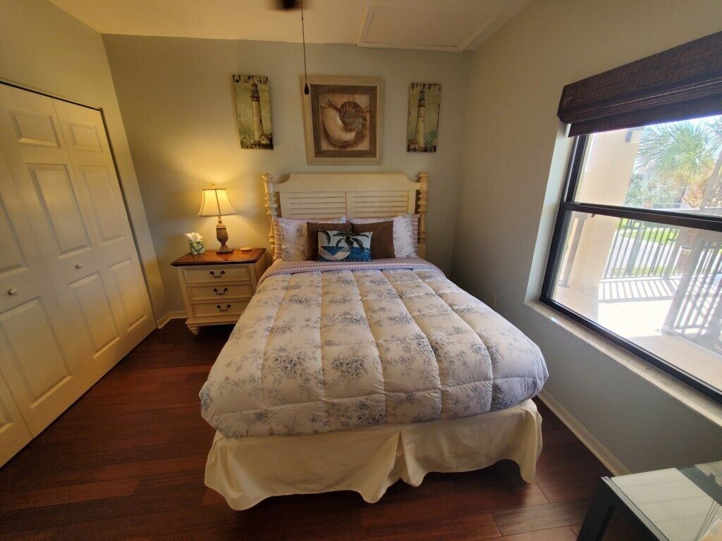 A bedroom with a bed, a nightstand, a lamp, and a window with a view of a fence.