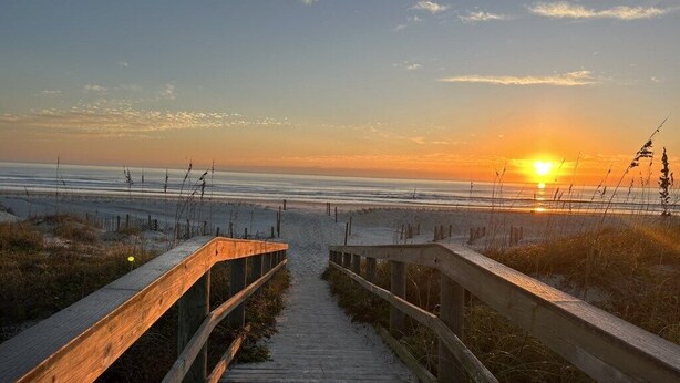 A wooden boardwalk leading to a beach with a sunset in the background. - Ocean Village Club I35 (St. Augustine)
