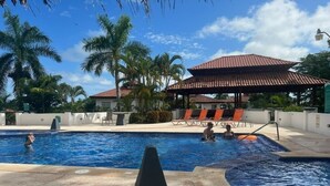 A swimming pool with lounge chairs and a covered area, surrounded by palm trees and a clear sky. - Ocean Village Club O15 (St. Augustine)