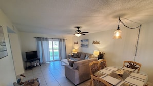 A living room with a sofa, TV, and dining area with chairs and a table. - Ocean Village Club O15 (St. Augustine)