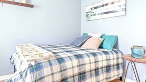 Ein Schlafzimmer mit einem Bett, einem kleinen Tisch, einer Ablage mit Dekoration und einem Wandbild.