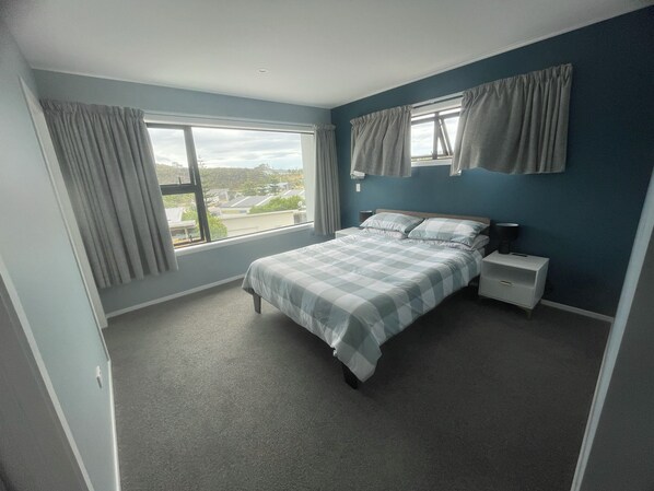 A bedroom with a large bed, a nightstand, a window with curtains, and a view of the outside.