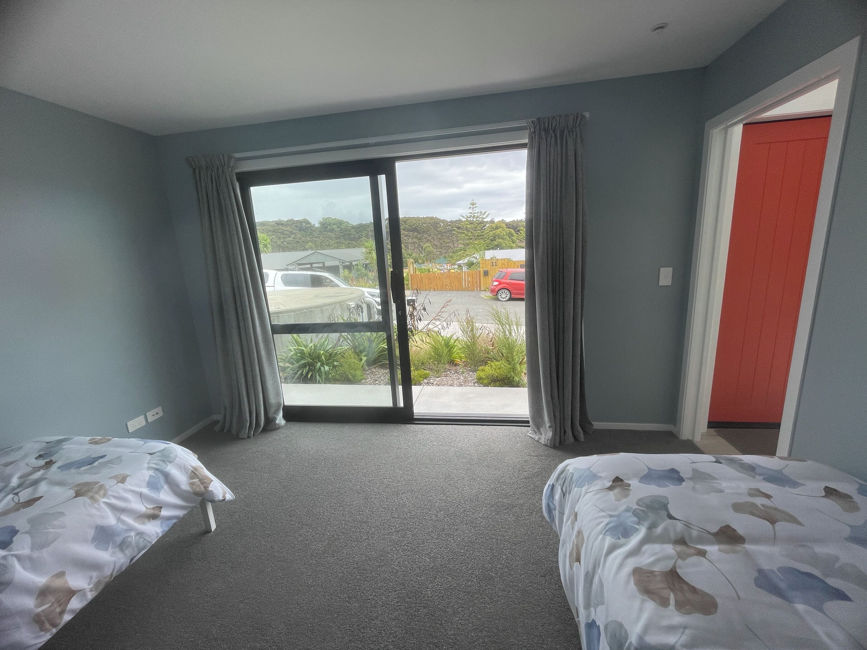 A room with two beds, a sliding glass door leading to a parking area, and a red door.