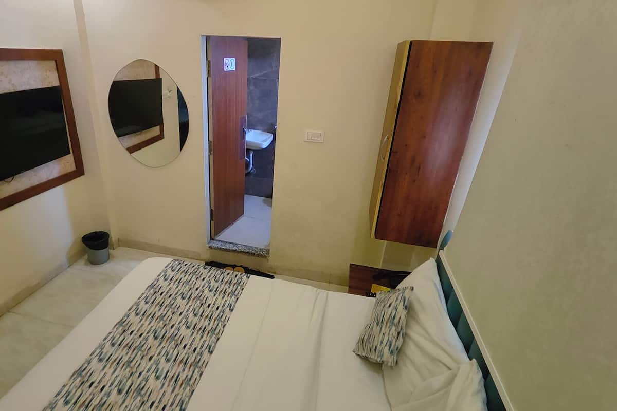 A bedroom with a bed, a TV, a mirror, and a wooden wardrobe.