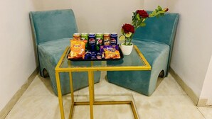 A glass-top table with snacks and drinks, a potted red rose, and two teal armchairs. - Hotel One Stay (Indore)