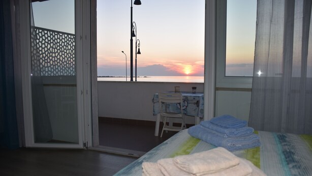 A room with a bed, a table with chairs, and a view of the sunset over the sea.
