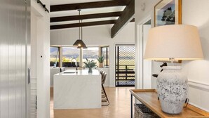 Une cuisine moderne dotée d’un îlot central, de poutres en bois et d’une grande fenêtre offrant une vue sur l’extérieur.