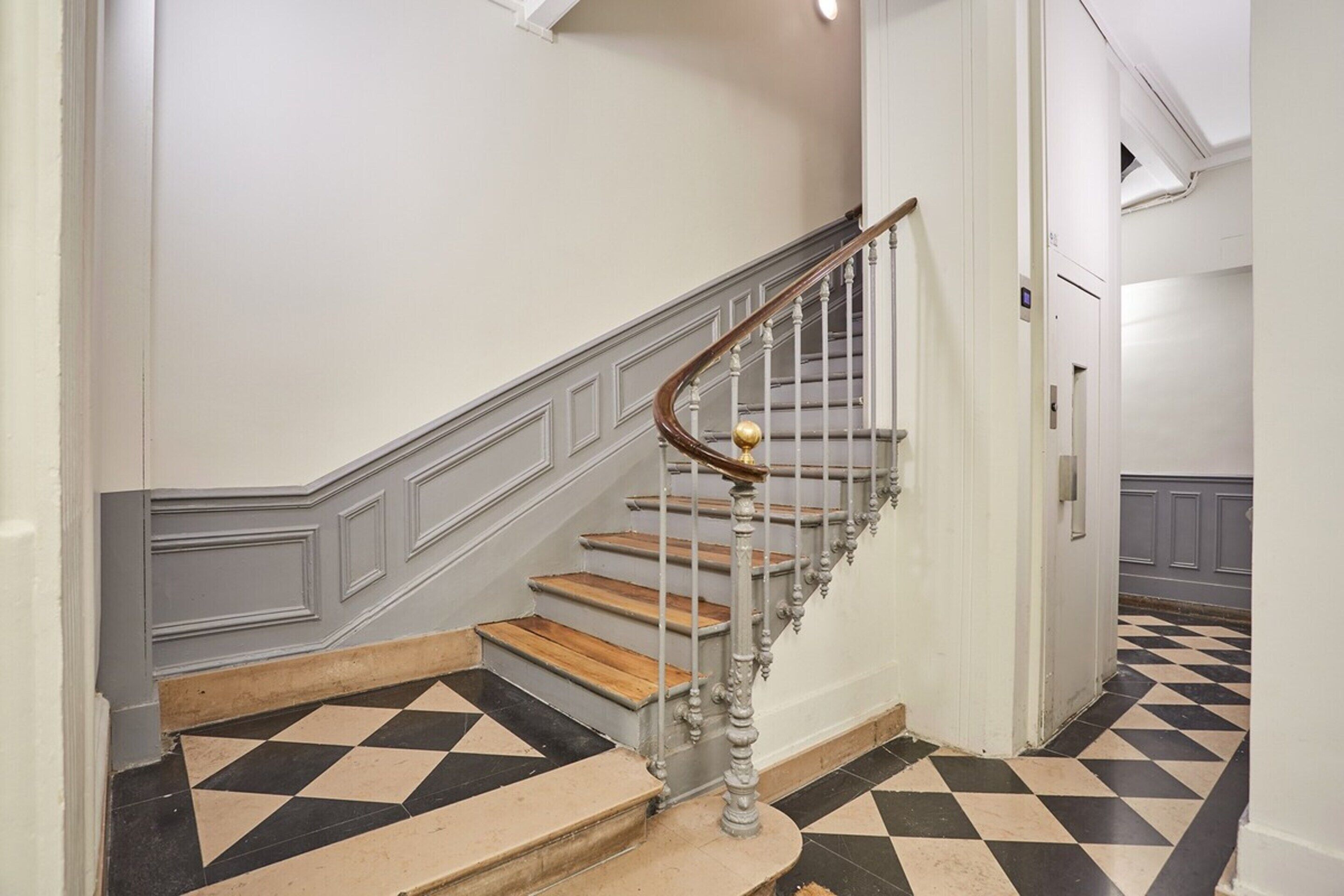 A staircase with a wooden handrail and a black and white checkered floor.