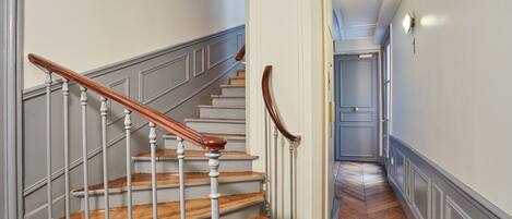 A staircase with wooden steps and white balusters, leading to a hallway with a herringbone floor pattern.