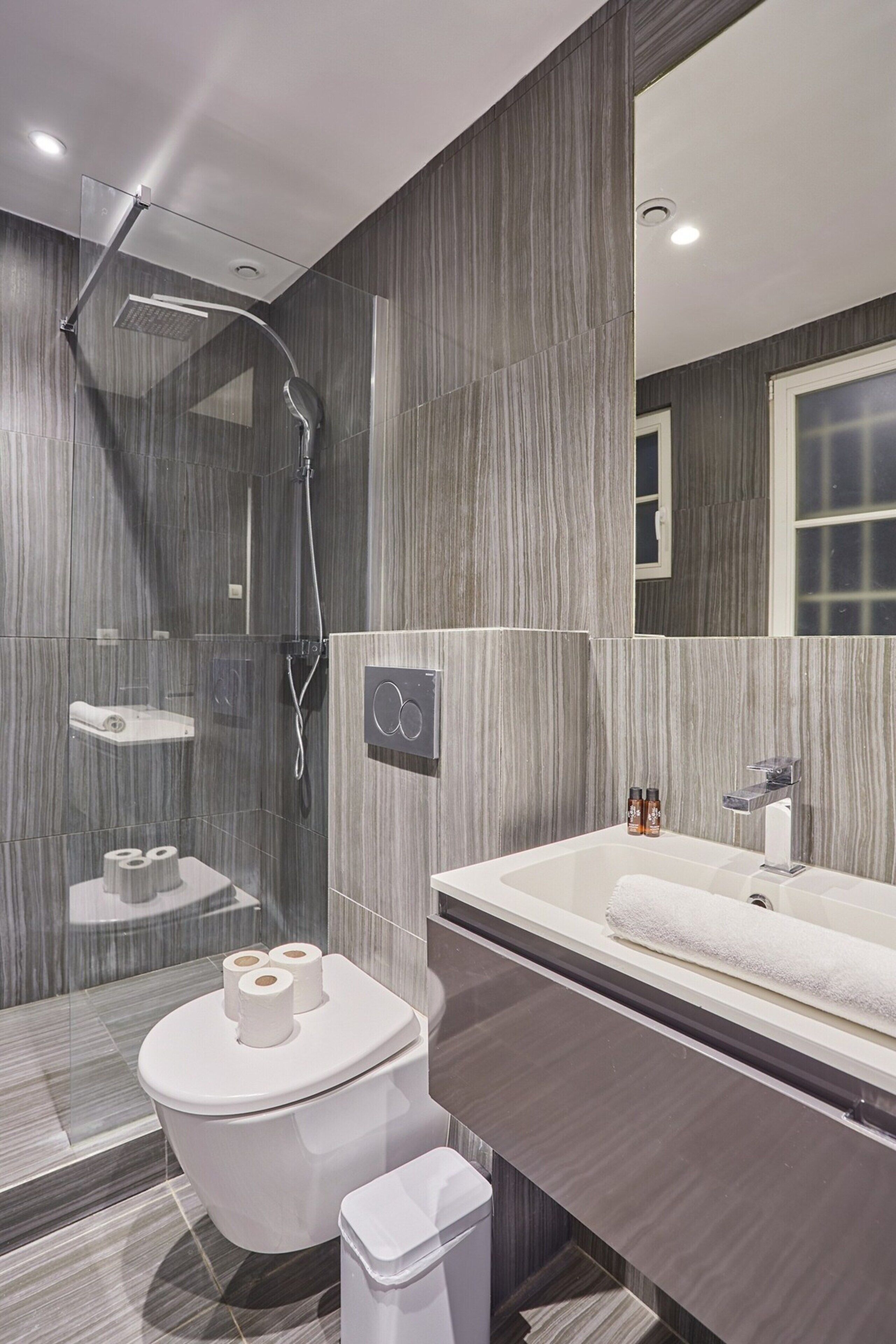 Un baño moderno con ducha envuelta en vidrio, inodoro blanco, tocador con espejo y perchero para toallas.