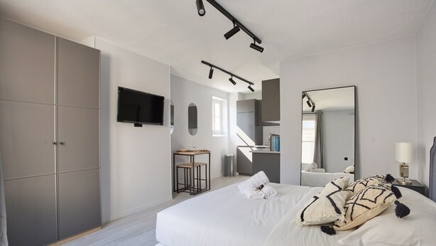 A modern bedroom with a large bed, a TV mounted on the wall, a desk, and a mirror. - Sublim Studio Beaubourg/le Marais (Paris)