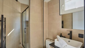 A modern bathroom with a glass shower enclosure, a toilet, and a sink with a towel. - Sublim Studio Beaubourg/le Marais (Paris)
