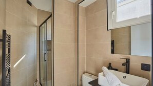 A modern bathroom with a glass shower enclosure, a toilet, and a sink with a towel. - Sublim Studio Beaubourg/le Marais (Paris)