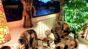 Una habitación acogedora con dos sillones cómodos, una mesita con un jarrón de flores y una ventana con vistas a un canal.