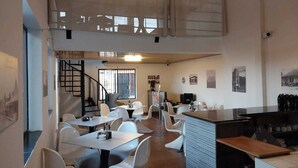 A modern dining area with white chairs and tables, a staircase, and a bar area with a counter and stools. - Hotel Nica Valley (Rivas)