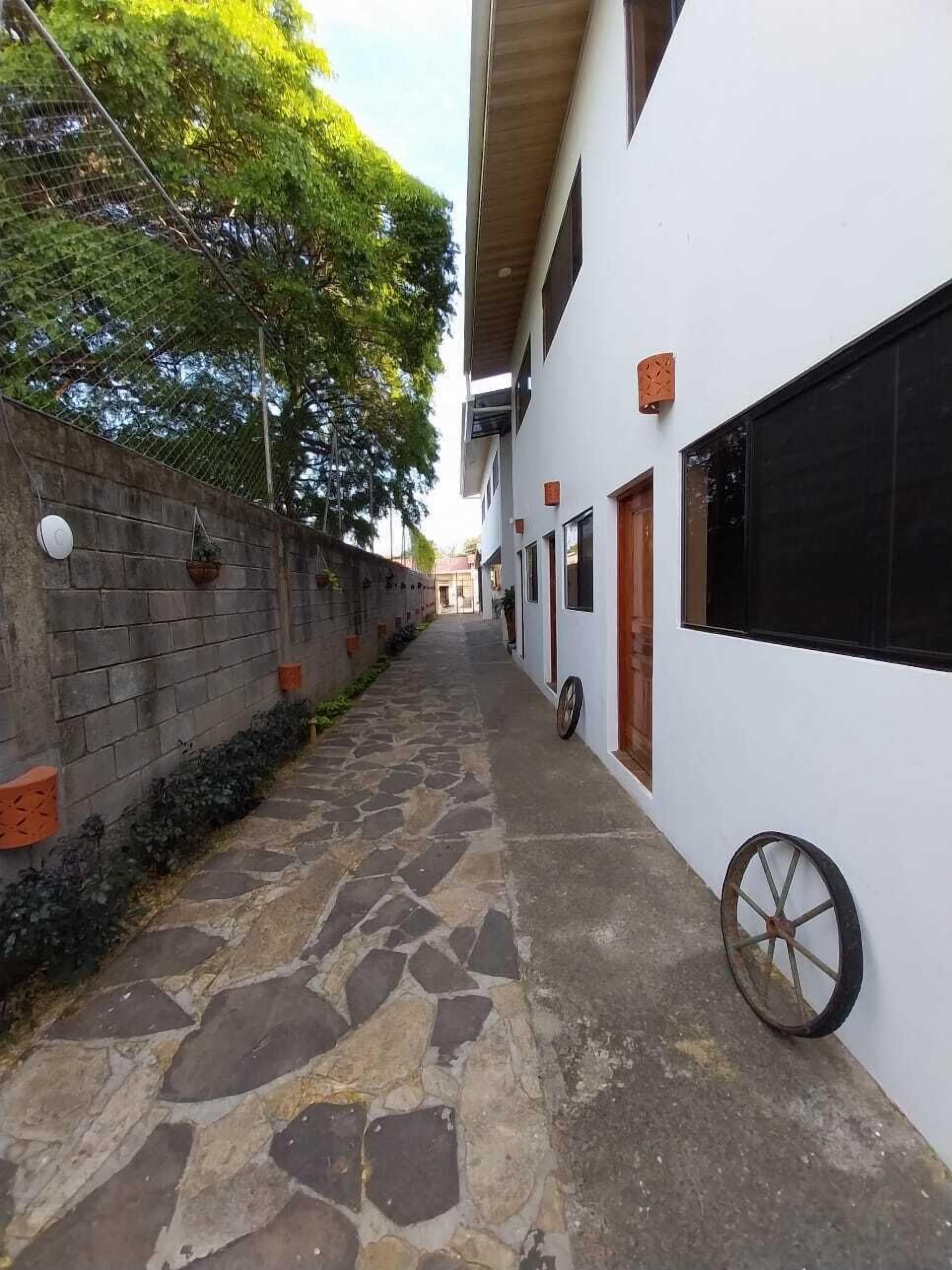 A narrow stone-paved alleyway flanked by a white building with a wooden door and a large window.