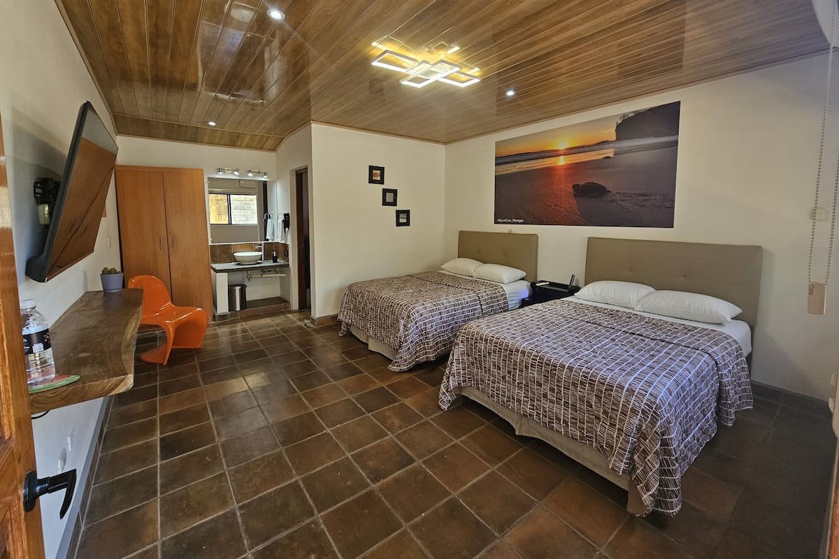 A hotel room with two beds, a bathroom, a desk, and a TV.