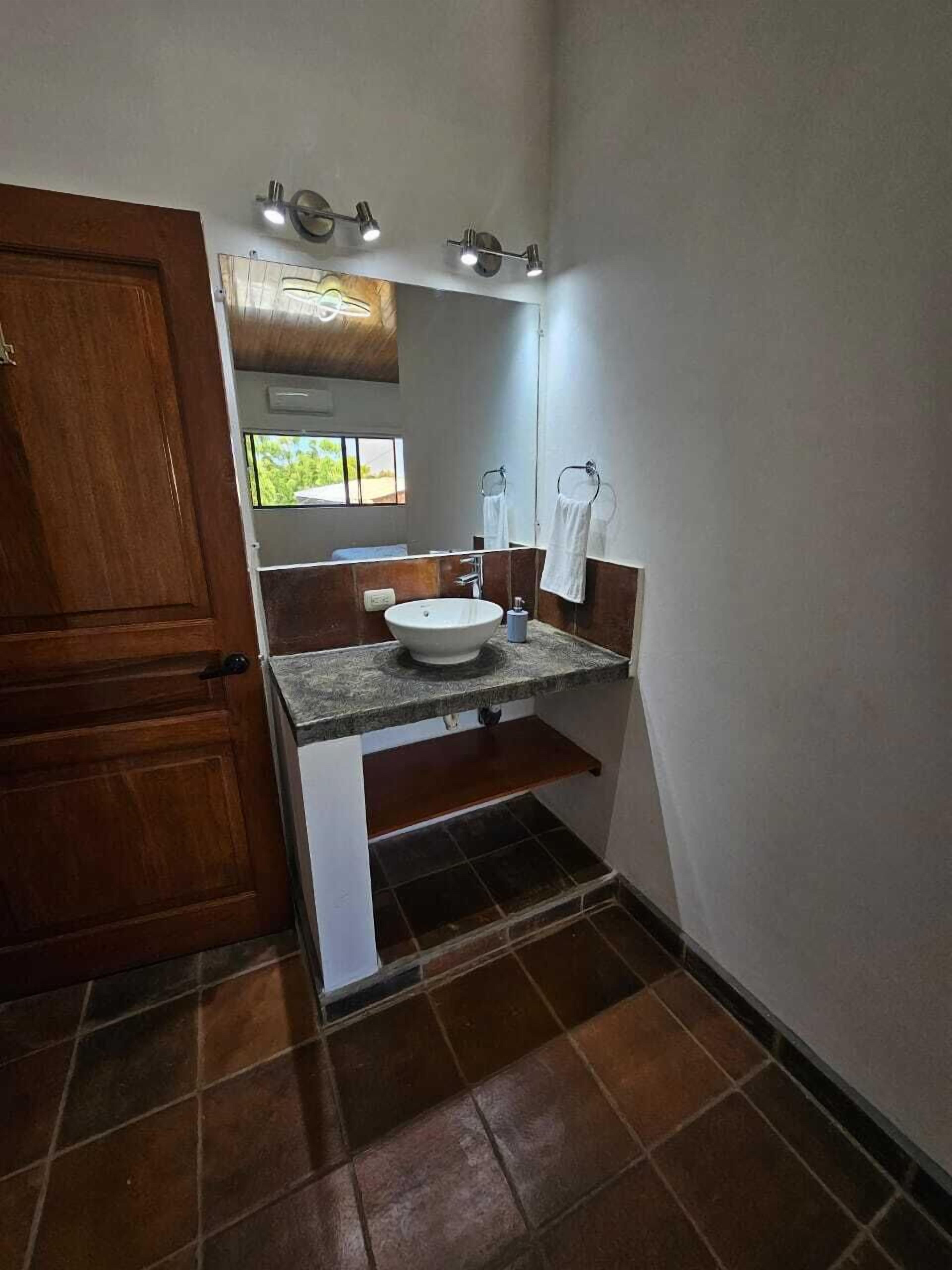 A bathroom with a wooden door, a white sink, a mirror, and a towel rack.
