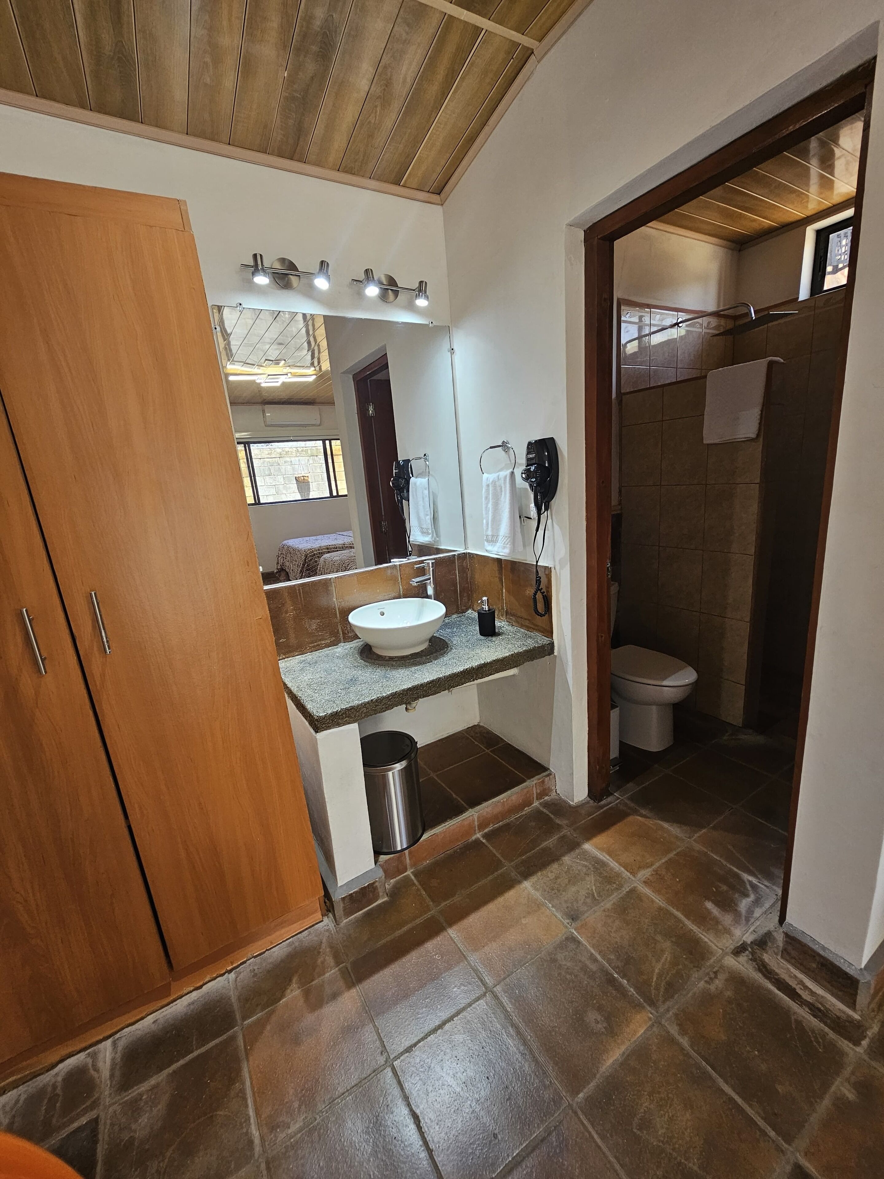 A bathroom with a wooden ceiling, a sink with a mirror, a towel rack, and a shower area.