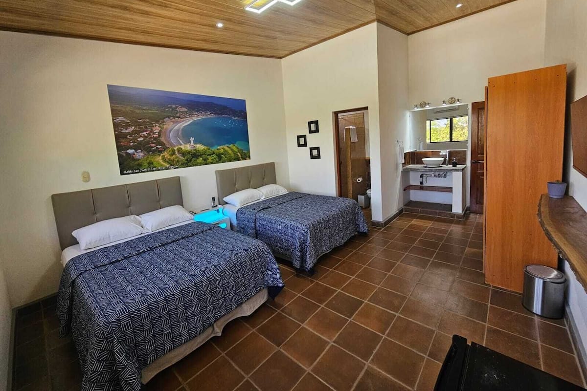 A hotel room with two beds, a bathroom, and a view of a coastal landscape.