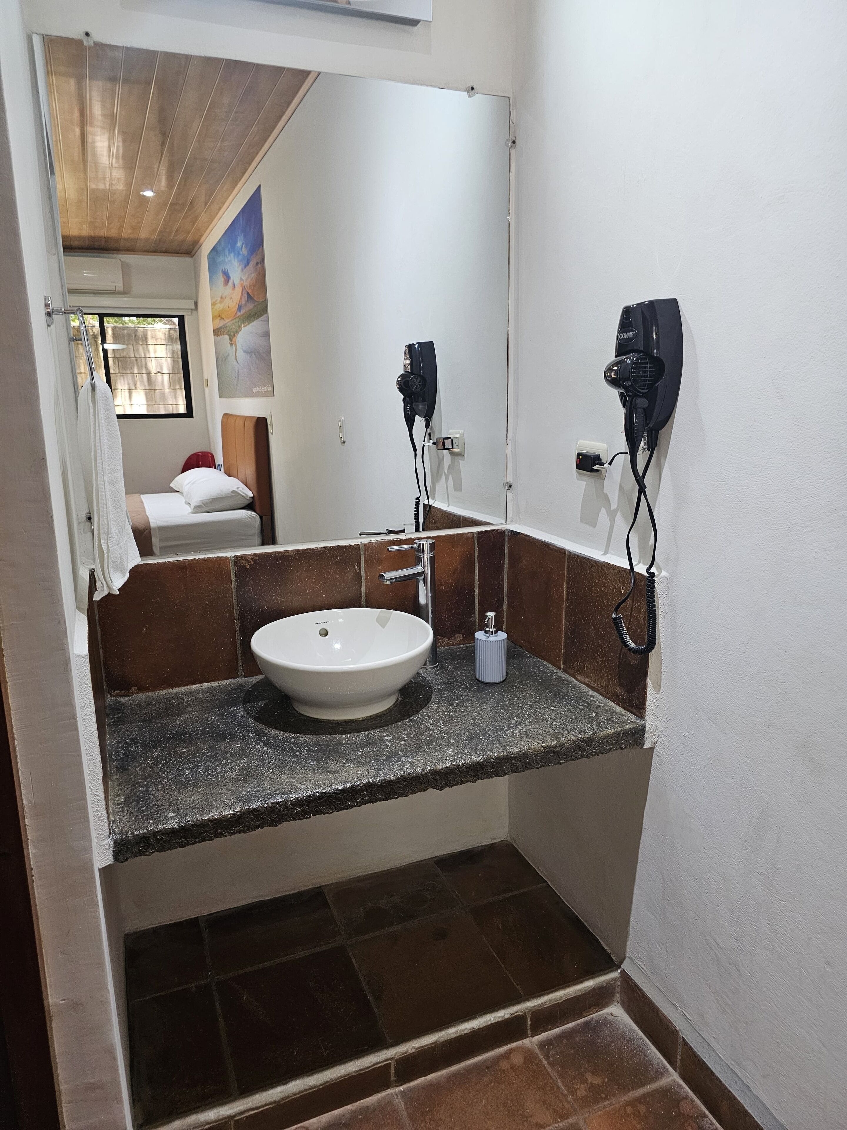 Un baño con un lavamanos blanco, un espejo y dos secadores de pelo fijados a la pared.