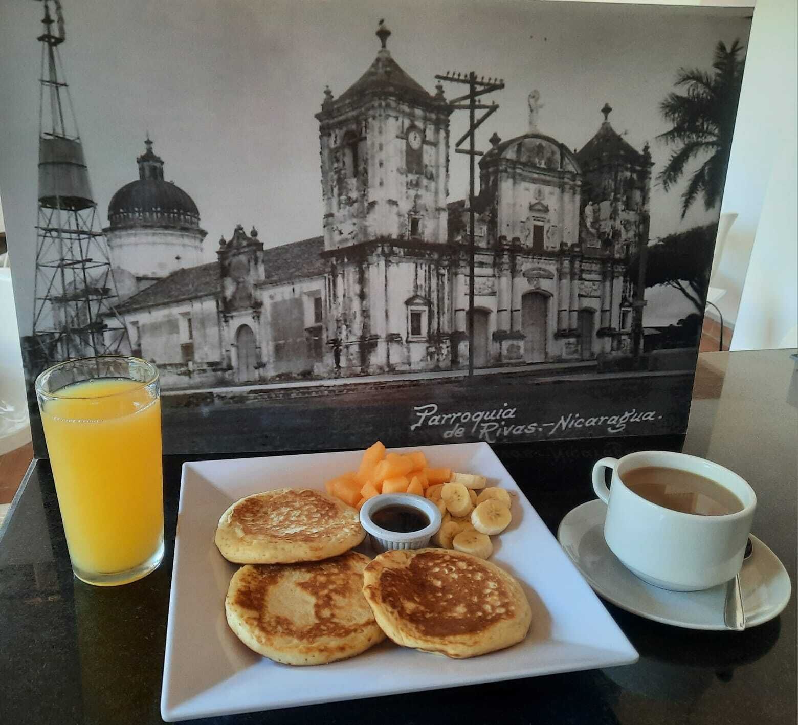 A breakfast plate with pancakes, fruit, and coffee, set against a backdrop of a historical building photo.