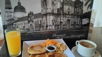 A breakfast plate with pancakes, fruit, and coffee, set against a backdrop of a historical building photo.