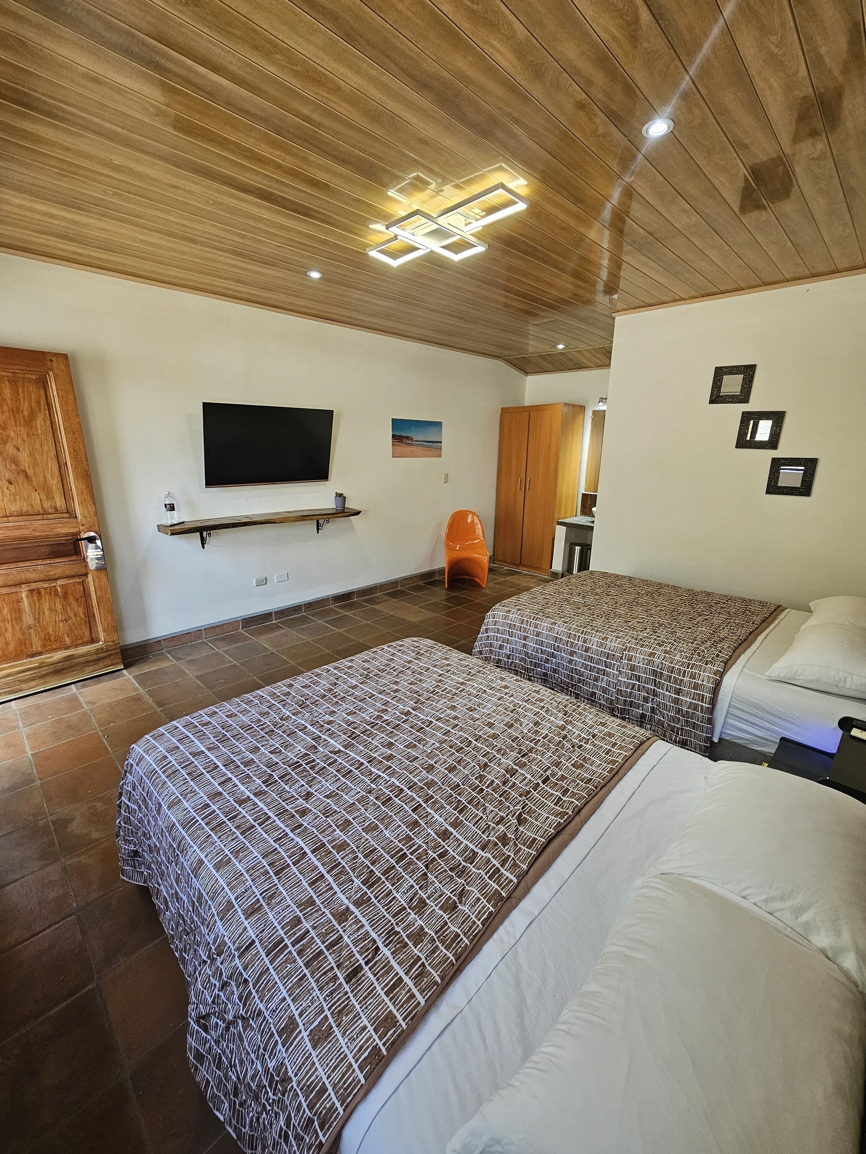 Habitación de hotel con dos camas, televisión, techo de madera y armario de madera.