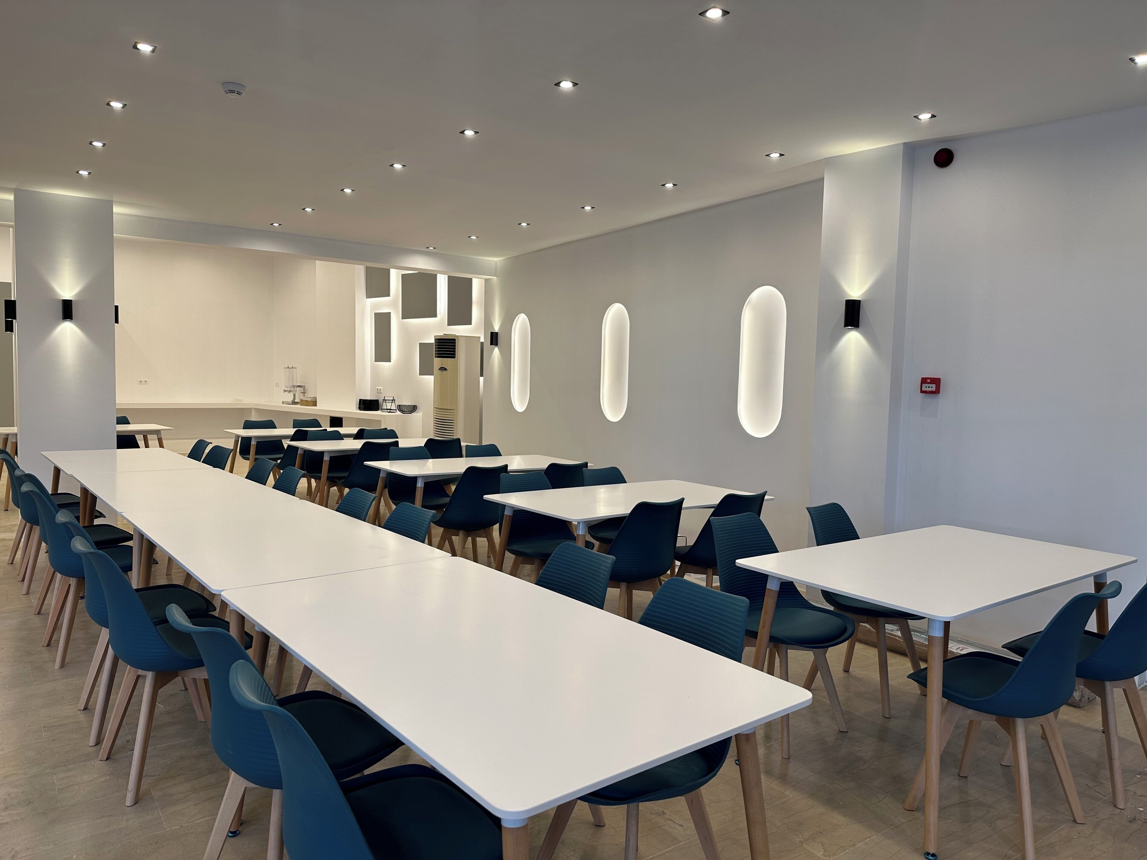 A modern conference room with white tables and blue chairs, recessed ceiling lights, and a whiteboard on the wall.