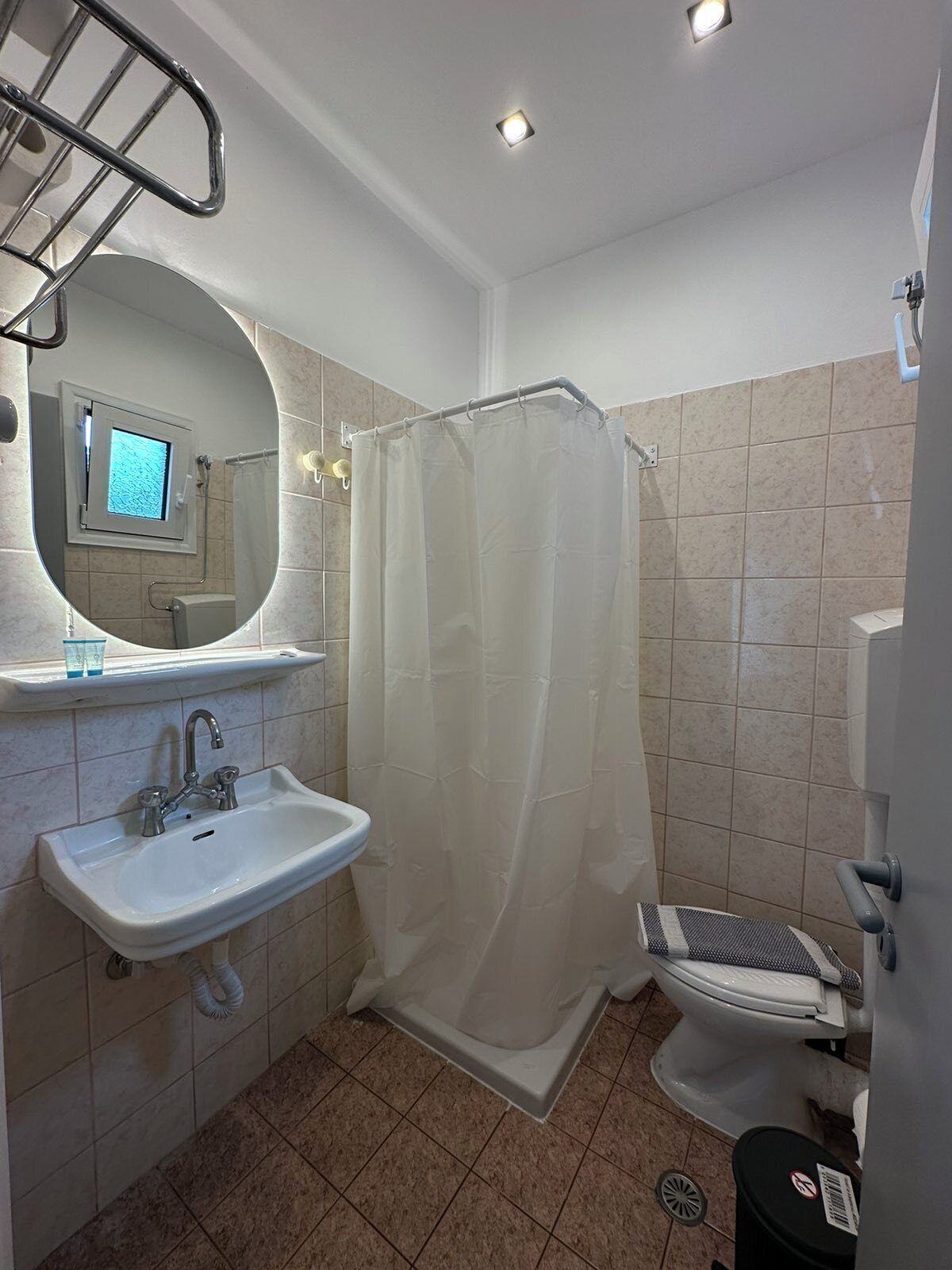 Un baño con lavamanos, espejo, cortina de ducha, inodoro y un ventanal pequeño.