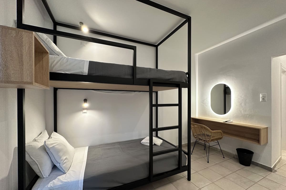 Una cama litera con escritorio y espejo, una silla y un cesto de basura pequeño.