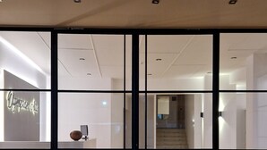 Der Eingang zum Olympian Alis Hotel mit einer Rezeption, einer Treppe zu den oberen Etagen und einer schwarzen Fußmatte mit dem Hotelnamen.