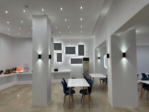 Moderni, hyvin valaistu ruokailutila, jossa on valkoiset seinät, upotetut kattovalaisimet ja keskellä oleva pöytä tuoleineen.