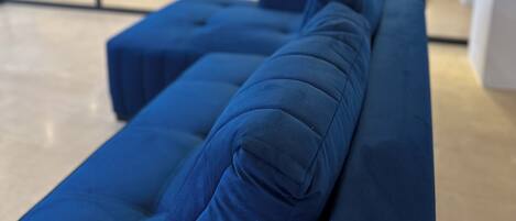 A modern lounge area with a long blue sofa and a glass partition.