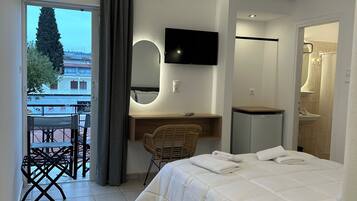 A modern hotel room with a bed, a desk with a chair, a TV mounted on the wall, and an air conditioning unit.