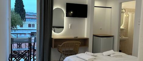 A modern hotel room with a bed, a desk with a chair, a TV mounted on the wall, and an air conditioning unit.