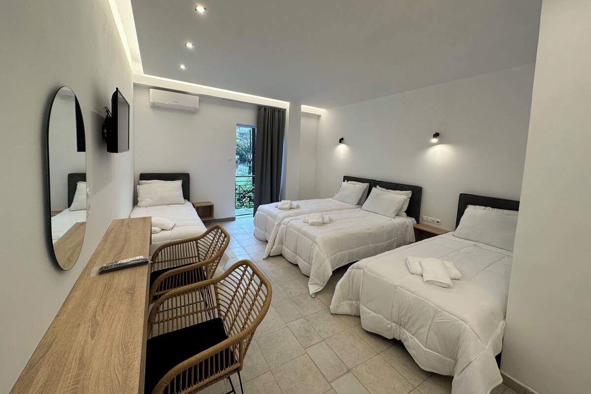 Una habitación de hotel con dos camas, un escritorio de madera, sillas de mimbre y un espejo grande.